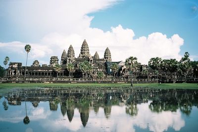 Angkor wat temple by lake against cloudy sky