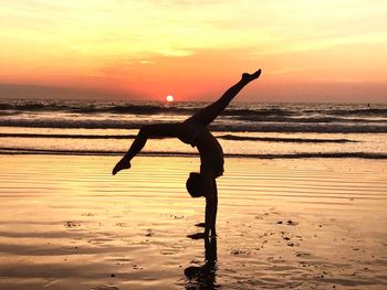 Side view of silhouette girl practicing handstand at beach during sunset