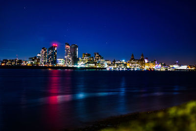 Illuminated buildings by river against sky at night