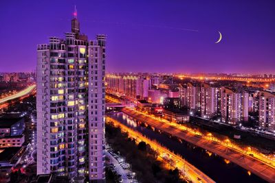 High-angle view of the urban landscape with the crescent moon hanging low in the evening sky.