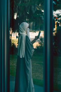 Reflection of a rear view of a muslim lady in a veil using phone on the window glass 