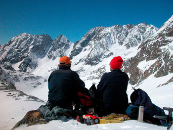 Rear view of people sitting on snowcapped mountain against sky