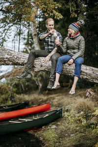 Full length of friends sitting on bench against trees