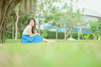 Portrait of smiling woman sitting on grass against trees