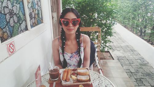 Portrait of woman wearing heart shape sunglasses having breakfast at sidewalk cafe