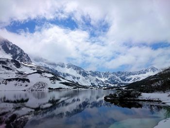 Scenic view of river amidst snowcapped mountains against cloudy sky