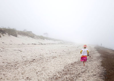 Rear view of girl walking on beach against sky