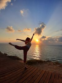 Woman dancing at beach against sky during sunset