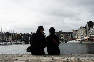 Rear view of couple sitting on boat at harbor