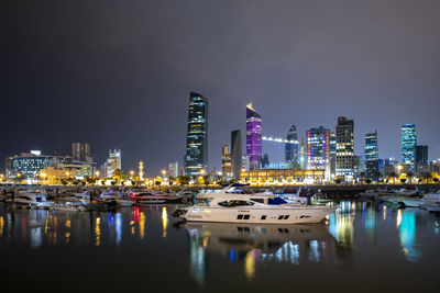 Illuminated buildings by river against sky at night