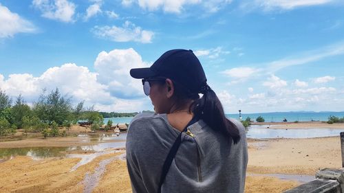 Young woman standing at beach against sky