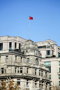 Low angle view of chinese flag on government building against clear blue sky