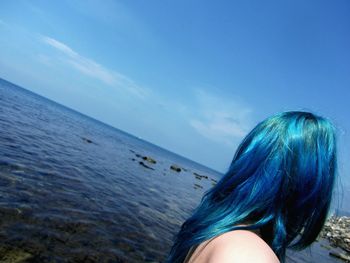 Rear view of woman standing at beach against blue sky