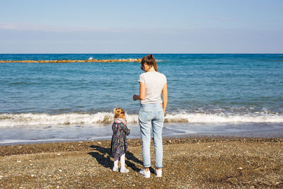 Rear view of woman standing on beach against sea