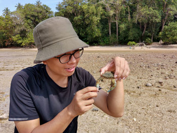 Portrait of man holding crab at beach with forest background