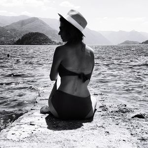 Rear view of woman standing in sea against mountains