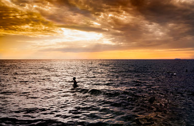 Silhouette person in sea against sky during sunset