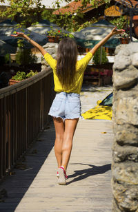 Rear view of mid adult woman with arms raised walking on footpath