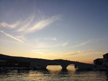 Bridge over river in city against sky during sunset