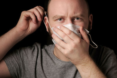 A young man with a beard and blue eyes puts on a medical mask 