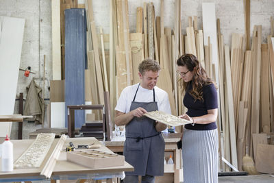 Female inspector and carpenter discussing inlay work while standing at workshop