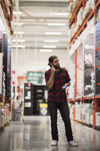 Full length of male customer talking through in-ear headphones at hardware store