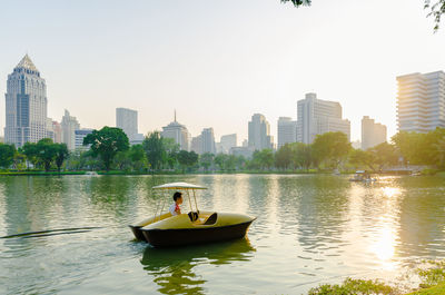 Man riding on paddle boat over lake by city against clear sky