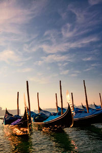 Gondolas moored in canal against cloudy sky during sunny day