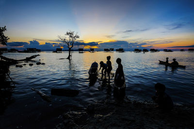 Silhouette children with boat in sea against sky during sunset