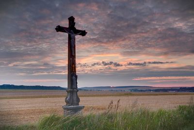 Cross on agricultural field against sky during sunset