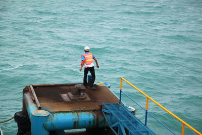 Rear view of man standing on metallic platform in sea