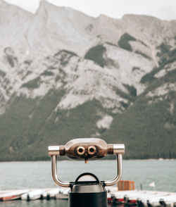 Close-up of coin-operated binoculars by sea against mountains