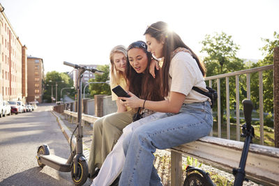 Young female friends spending time together outdoors and using phone