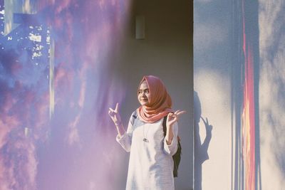 Young woman gesturing while standing by wall