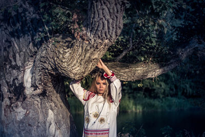 Portrait of woman standing by tree trunk