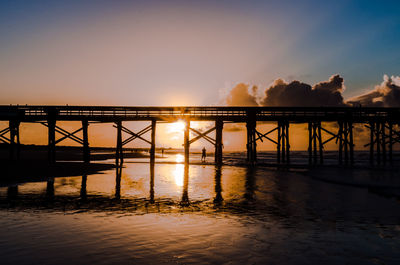 Silhouette bridge over sea against sky during sunset