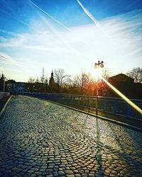 Footpath by street against sky during sunset