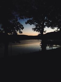 Silhouette trees by lake against sky during sunset