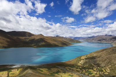 View of patched land with mountains and lake against cloudy sky