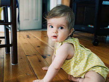 Portrait of cute baby girl sitting on hardwood floor at home