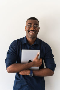 Positive african american adult male in formal clothes and eyeglasses standing with netbook in hands and looking at camera on white background