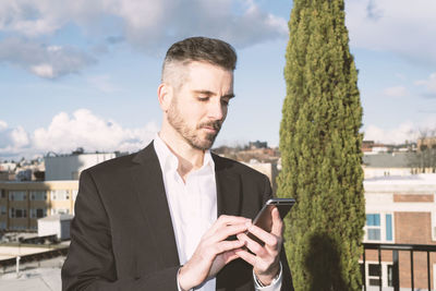 Businessman using phone against sky