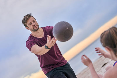 Trainer assisting woman exercising with medicine ball at beach