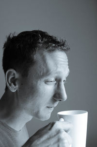 Close-up of young woman drinking coffee against gray background