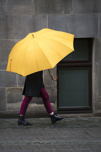 Low section of person carrying yellow umbrella on footpath during rain