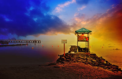 Lighthouse by sea against sky during sunset