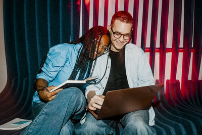 Happy businesswoman leaning on male colleague sitting with laptop