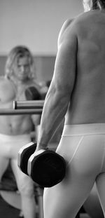Shirtless man lifting dumbbell reflecting on mirror at gym
