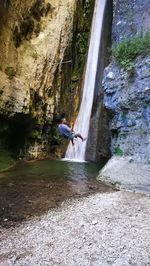 Man surfing on rock against waterfall