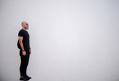 Full length of man in black floating against a white wall with copy space